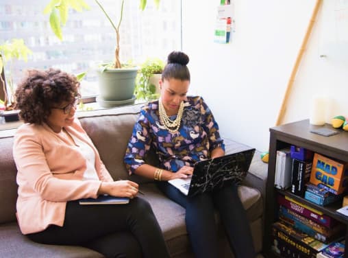 Duas mulheres conversando em uma sala confortável olhando para um notebook